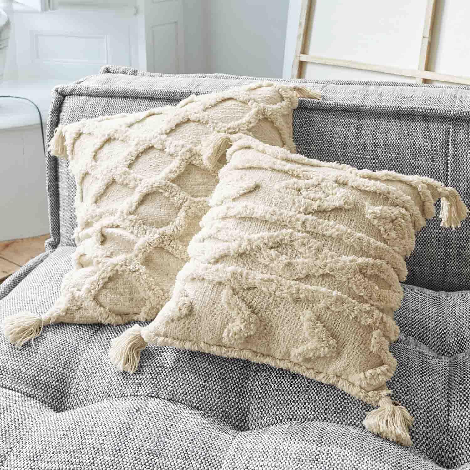 Cuscini decorativi beige in cotone con nappine su divano grigio, trama e motivo tessuto