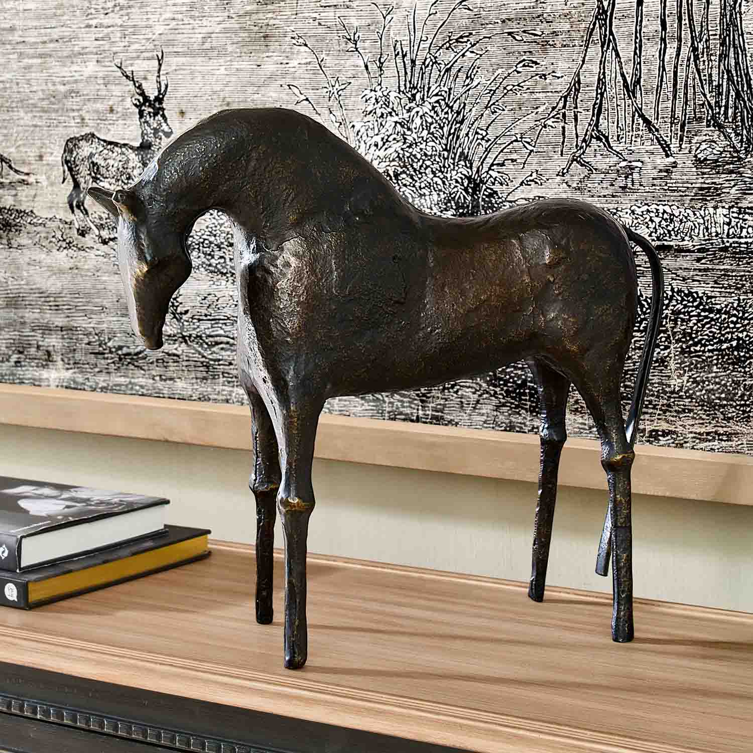 Scultura decorativa di cavallo in metallo scuro su piano in legno con libri accanto