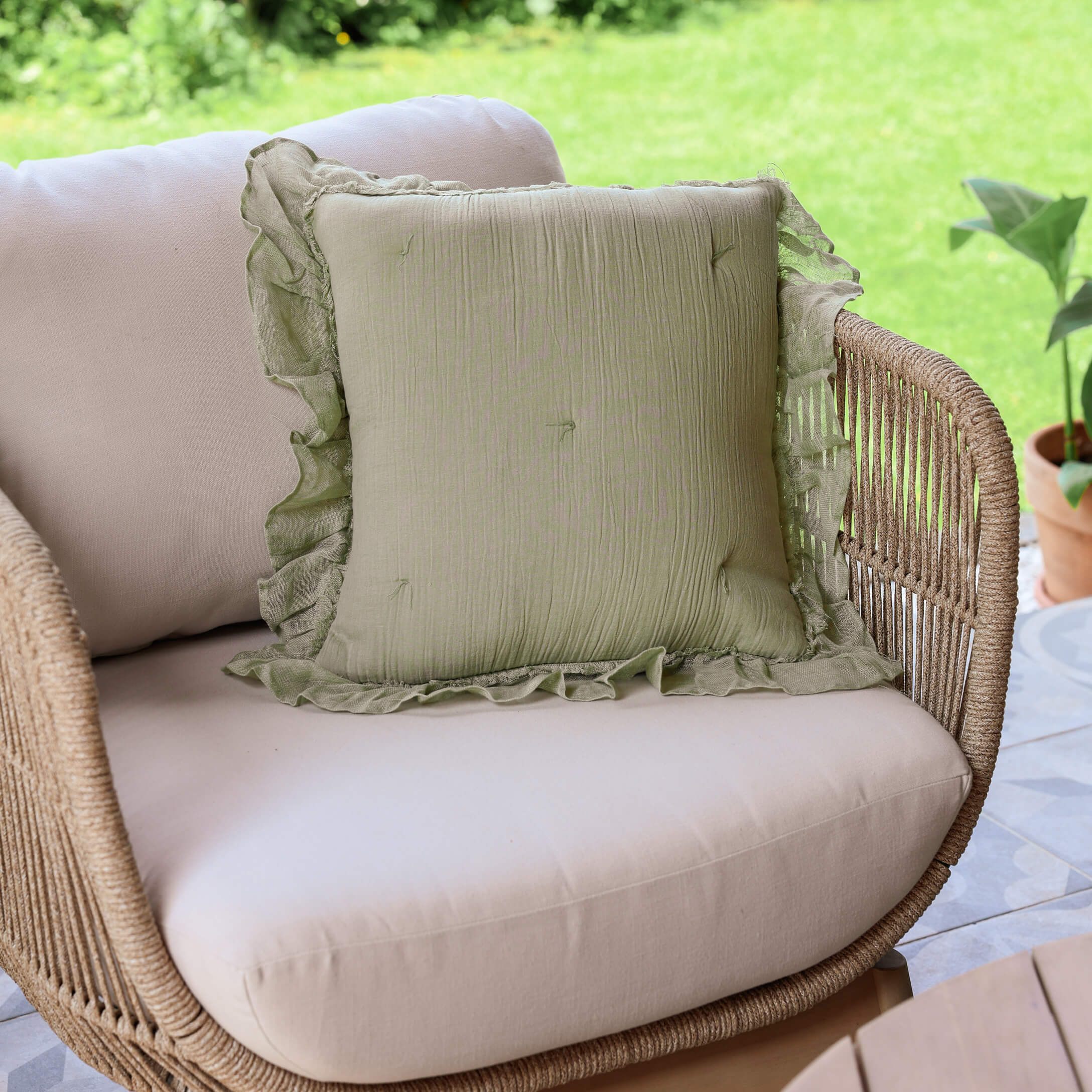 Cuscino decorativo verde in lino con volant su divano beige in rattan su terrazza