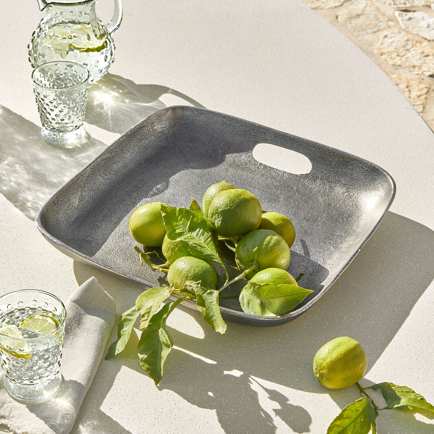 Vassoio quadrato in metallo grigio con lime verdi su tavolo chiaro, decorazione estiva da tavola