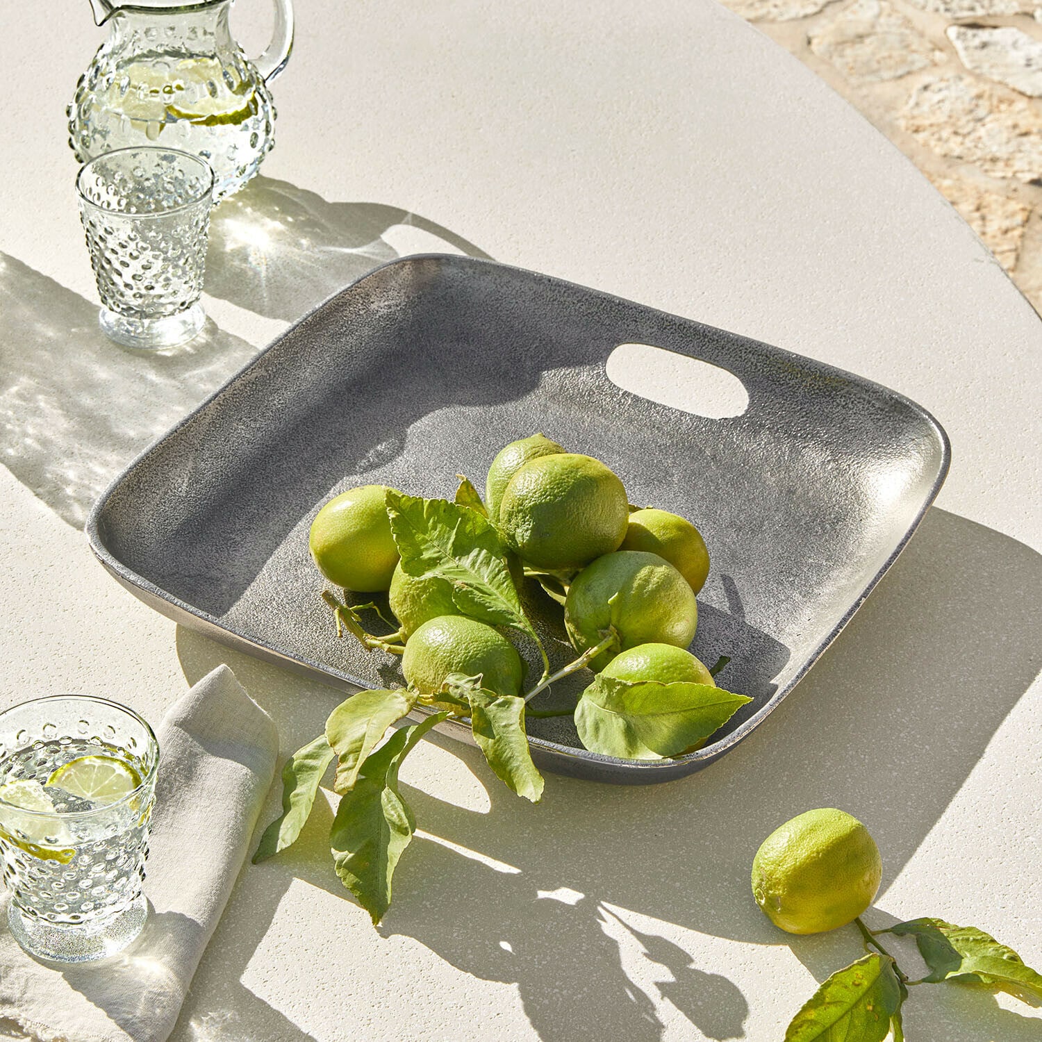 Vassoio Tarevo Vassoio quadrato in metallo grigio con lime verdi su tavolo chiaro, decorazione estiva da tavola