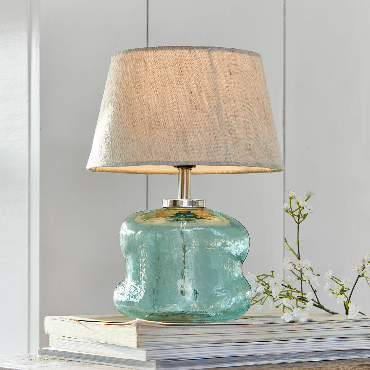 Lampada da tavolo Rufino Lampada da tavolo in vetro azzurro con paralume beige su pila di libri, decorazione d'interni
