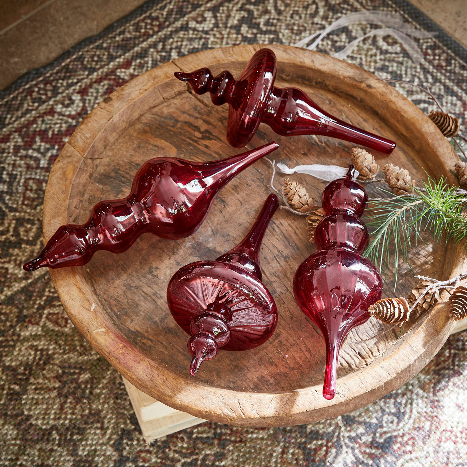 Set di 4 decorazioni da appendere Camorita Quattro decorazioni natalizie in vetro rosso su un vassoio di legno con pigne e rametti naturali