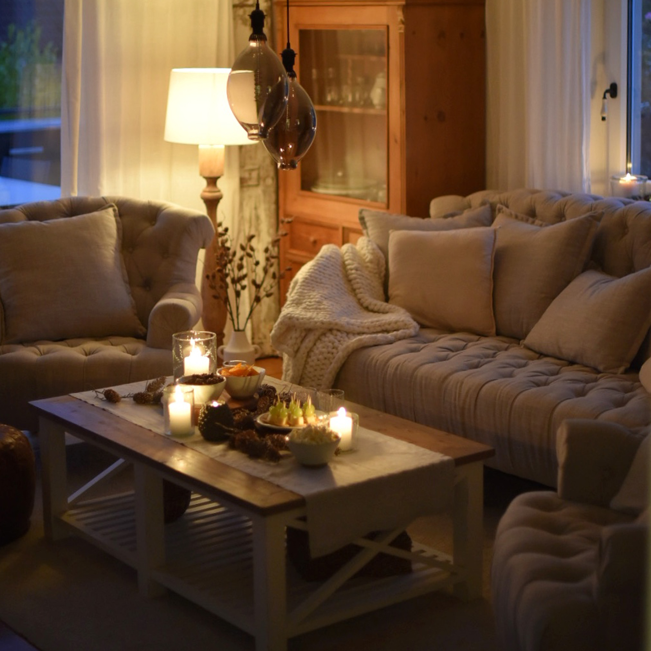Soggiorno accogliente con divano beige, poltrone e tavolino in legno con candele e snack