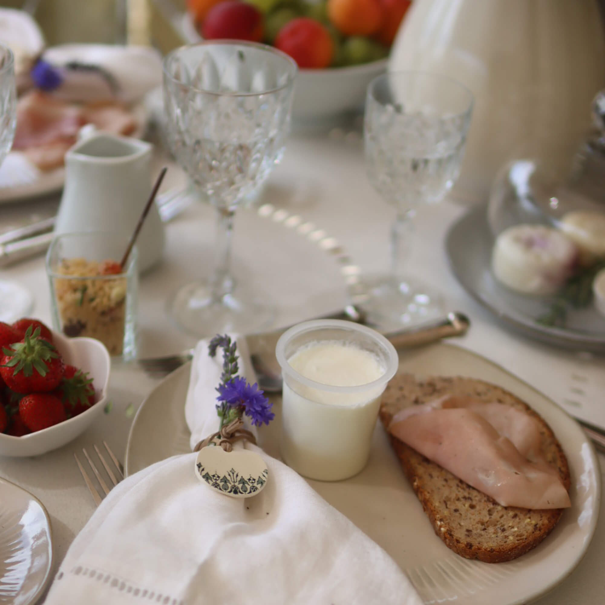Tavola per colazione con pane integrale, prosciutto e yogurt su piatto, tovagliolo decorato con fiori