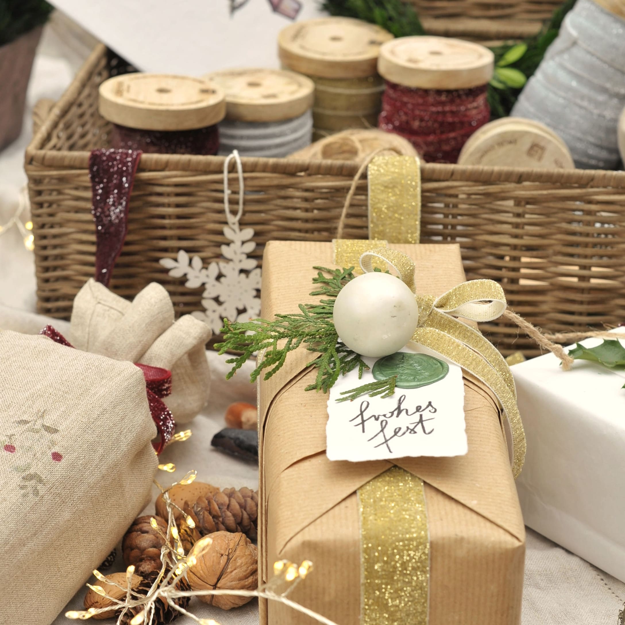 Regalo avvolto in carta marrone con nastro dorato e decorazioni verdi, sullo sfondo bobine di nastri