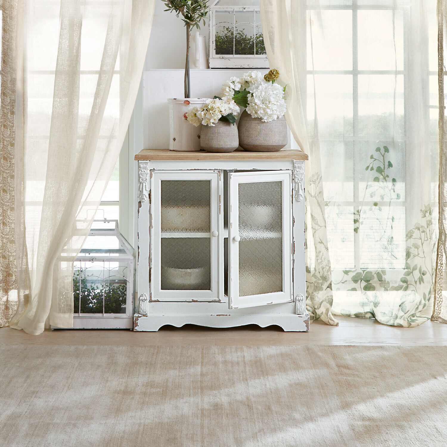 Mobile con ante in vetro South Yarmouth Mobile in legno bianco con ante in vetro e vasi decorativi con fiori in interno luminoso
