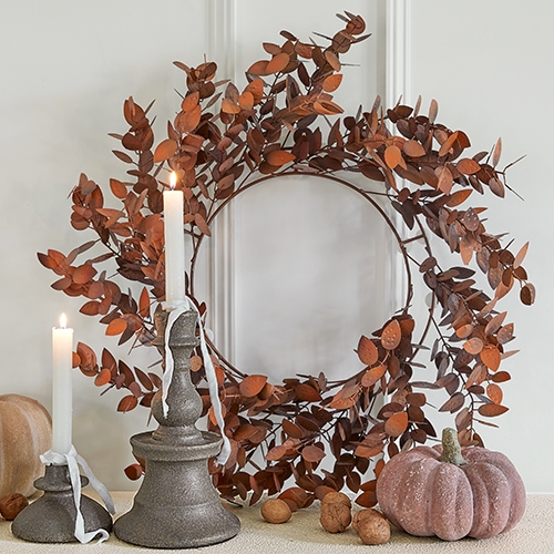 Corona decorativa in metallo arrugginito con due candele e zucca decorativa su tavolo