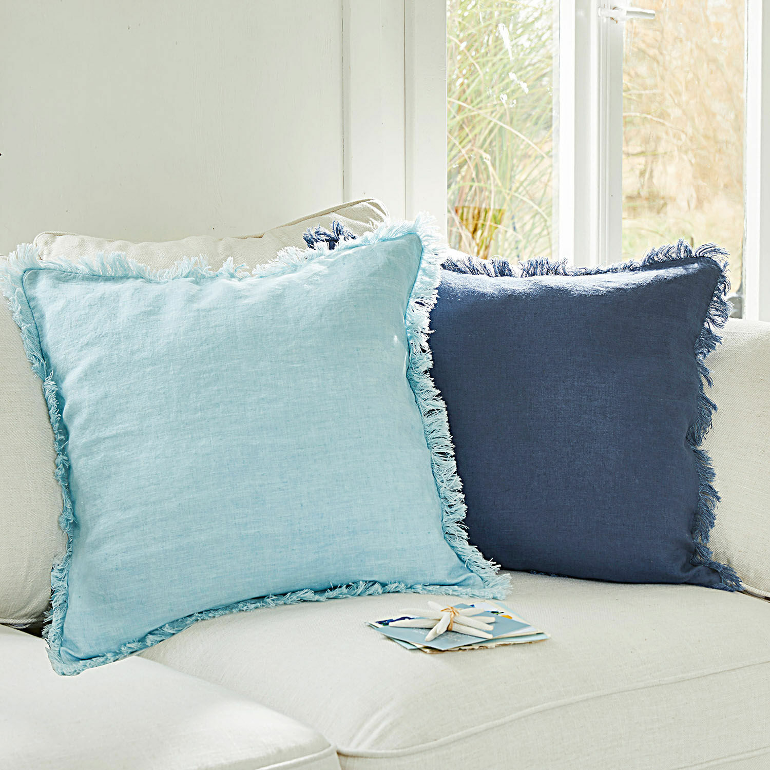 Coppia di copricuscini Quebo Set di due cuscini decorativi in lino azzurro chiaro e blu scuro con frange su divano chiaro