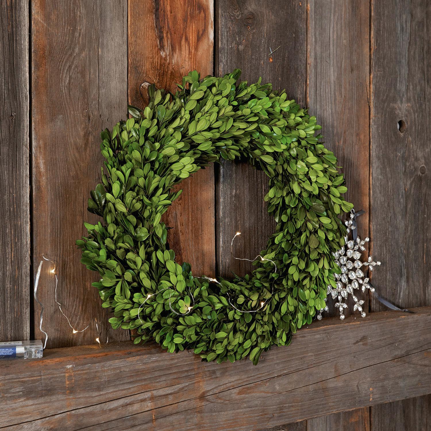 Ghirlanda Myrcella Corona verde di bosso su sfondo in legno con luci LED e decorazione a fiocco di neve scintillante