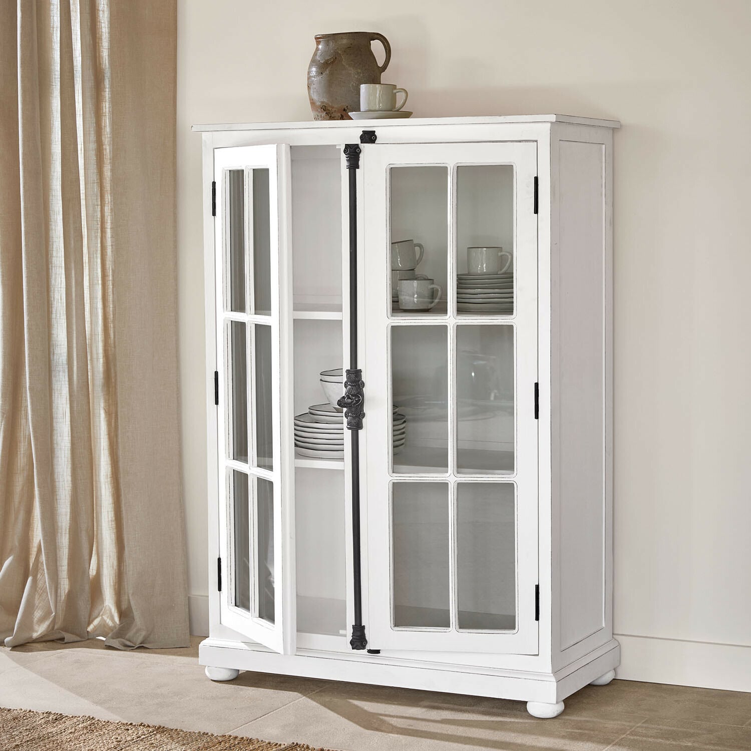 Credenza Salivonne Vetrina in legno bianco con ante in vetro e maniglie in metallo nero stile vintage in ambiente luminoso
