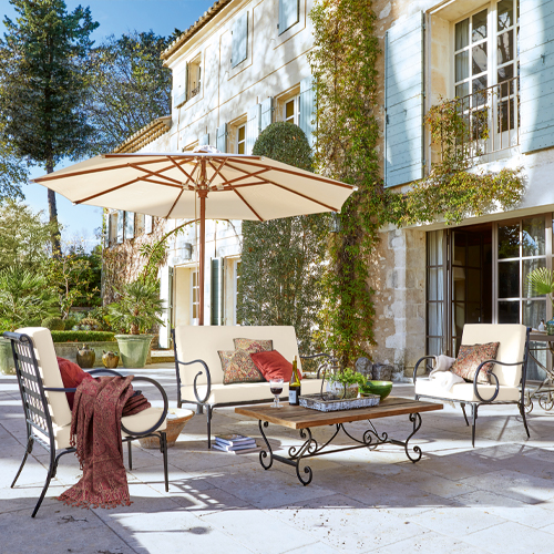 Set di mobili da giardino con struttura in metallo e cuscini crema su terrazza in pietra con ombrellone