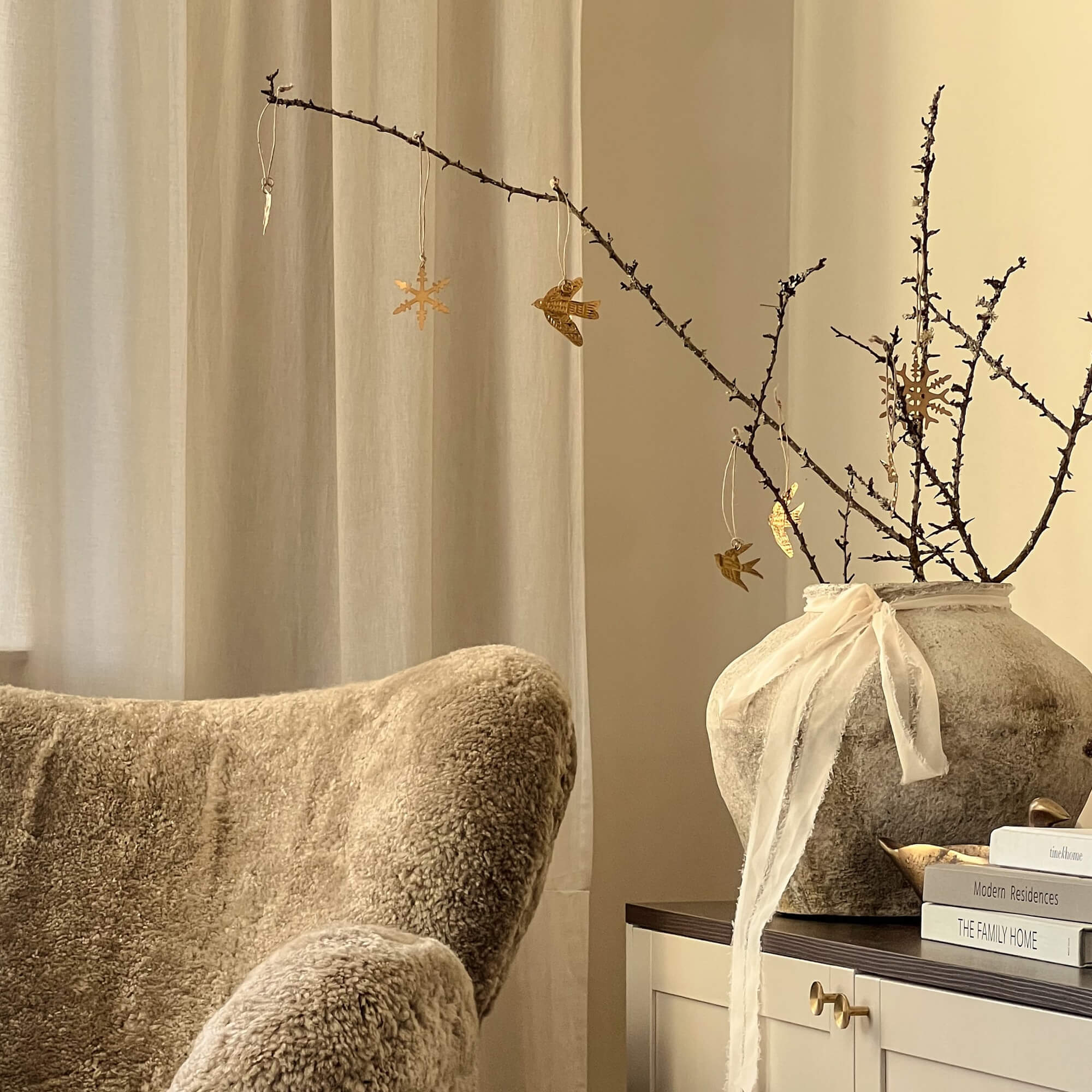 Angolo accogliente con poltrona beige in pelliccia sintetica e vaso decorativo con rami e ornamenti dorati