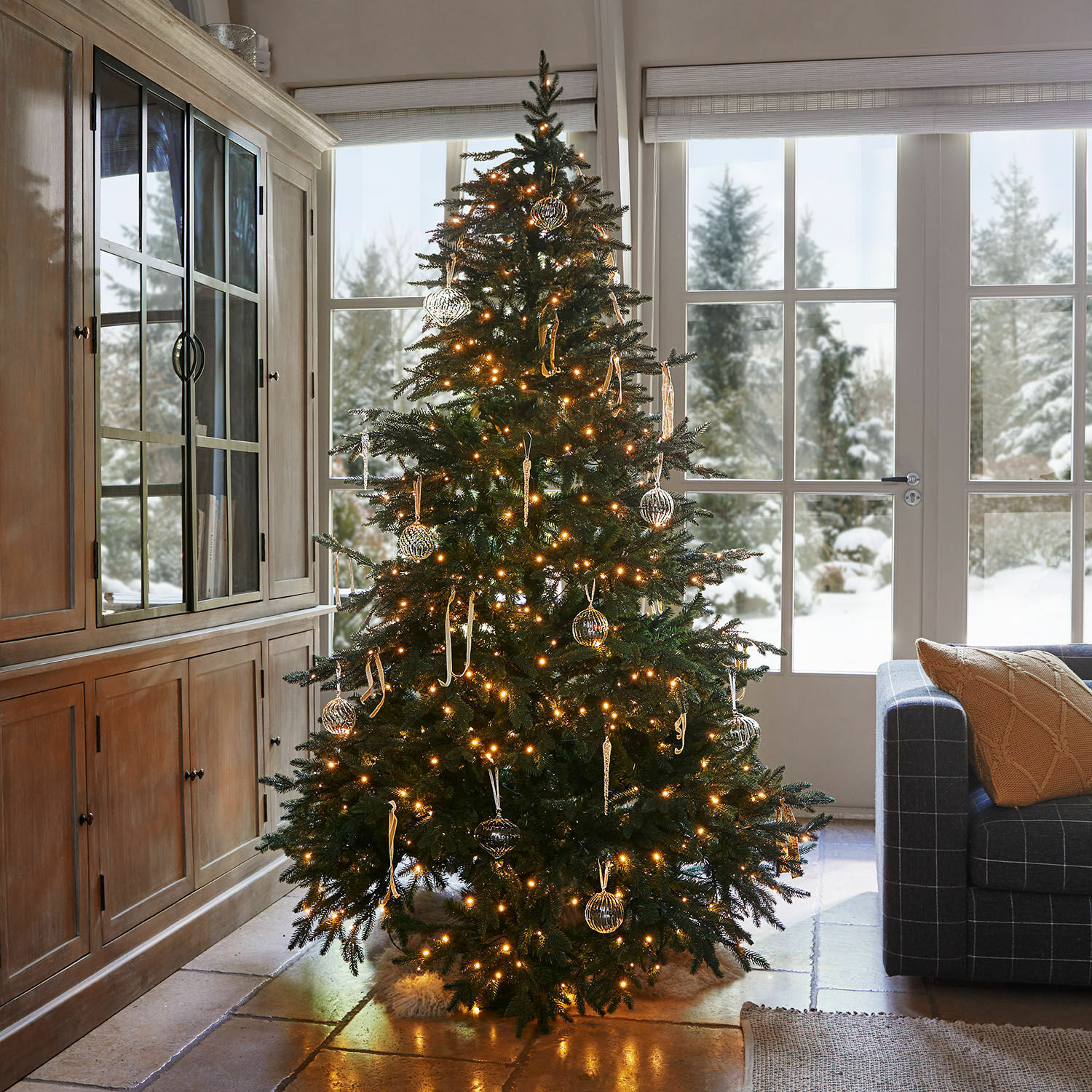 Albero di Natale Celindor Albero di Natale illuminato con rami verdi e decorazioni in vetro in soggiorno accogliente con vista sulla neve