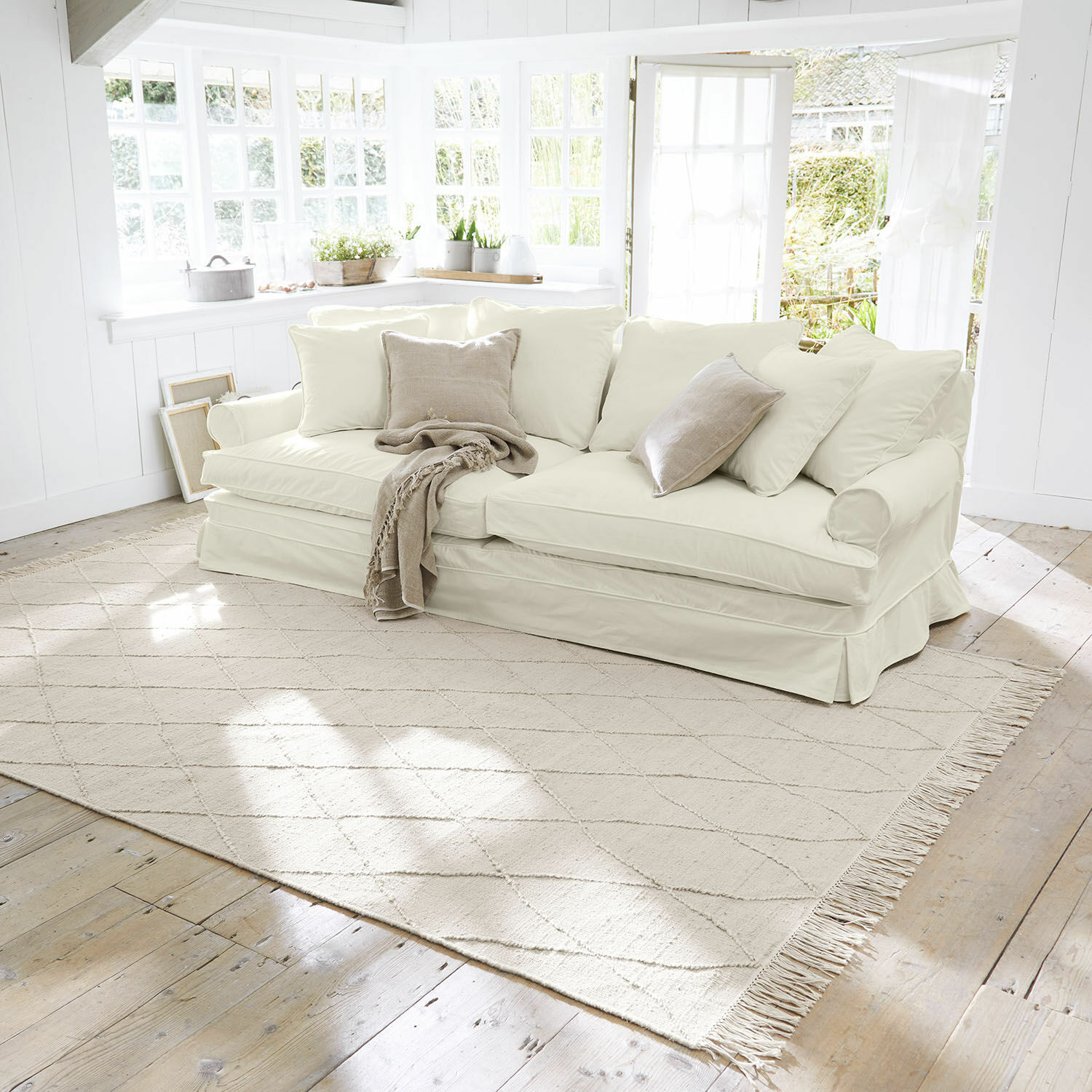 Tappeto Ivonique Divano beige chiaro con cuscini morbidi e coperta in soggiorno luminoso e accogliente