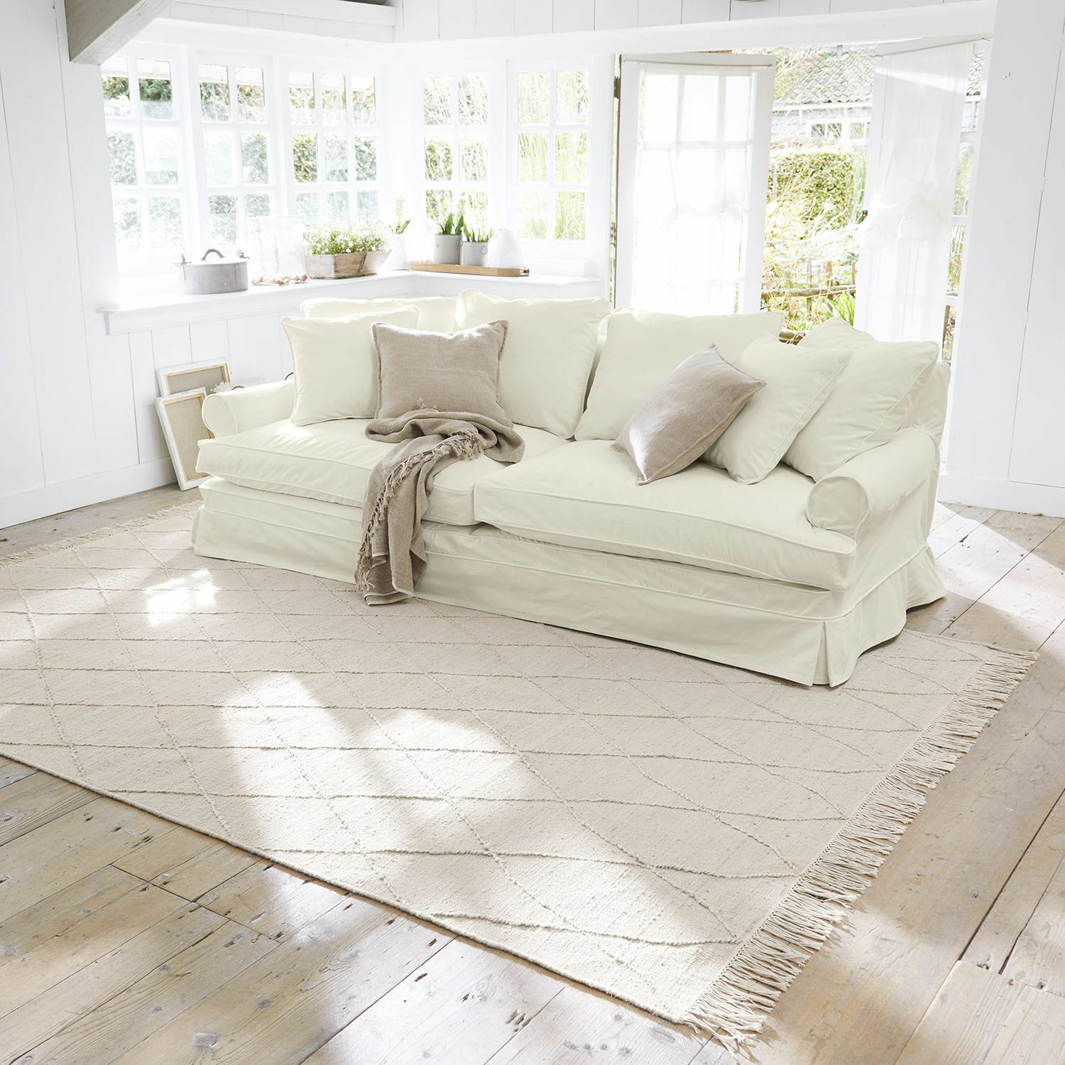 Tappeto Ivonique Divano beige chiaro con cuscini morbidi e coperta in soggiorno luminoso e accogliente