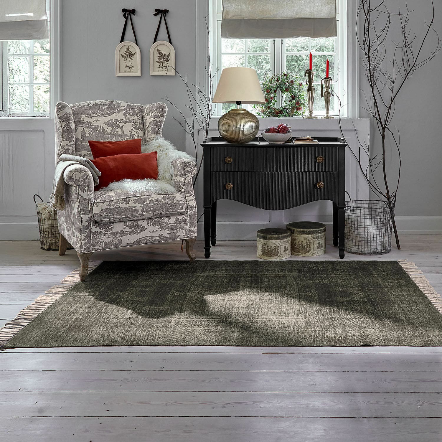 Tappeto per interni ed esterni Belaric Poltrona accogliente beige con motivo grigio e cuscini rossi accanto a comò nero vintage in soggiorno luminoso