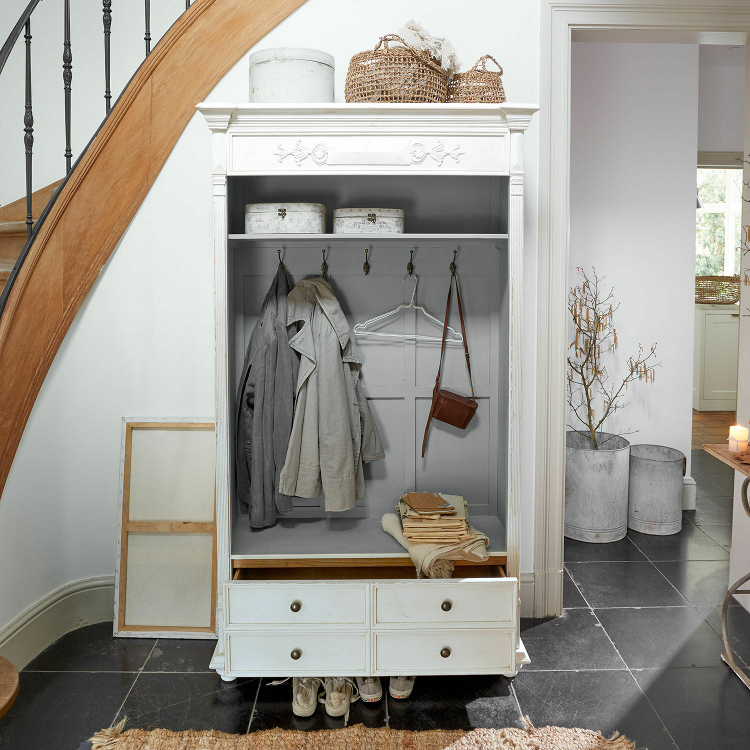 Armadio Étourville Armadio bianco in legno con ganci, cassetti e cesti decorativi in un ingresso luminoso