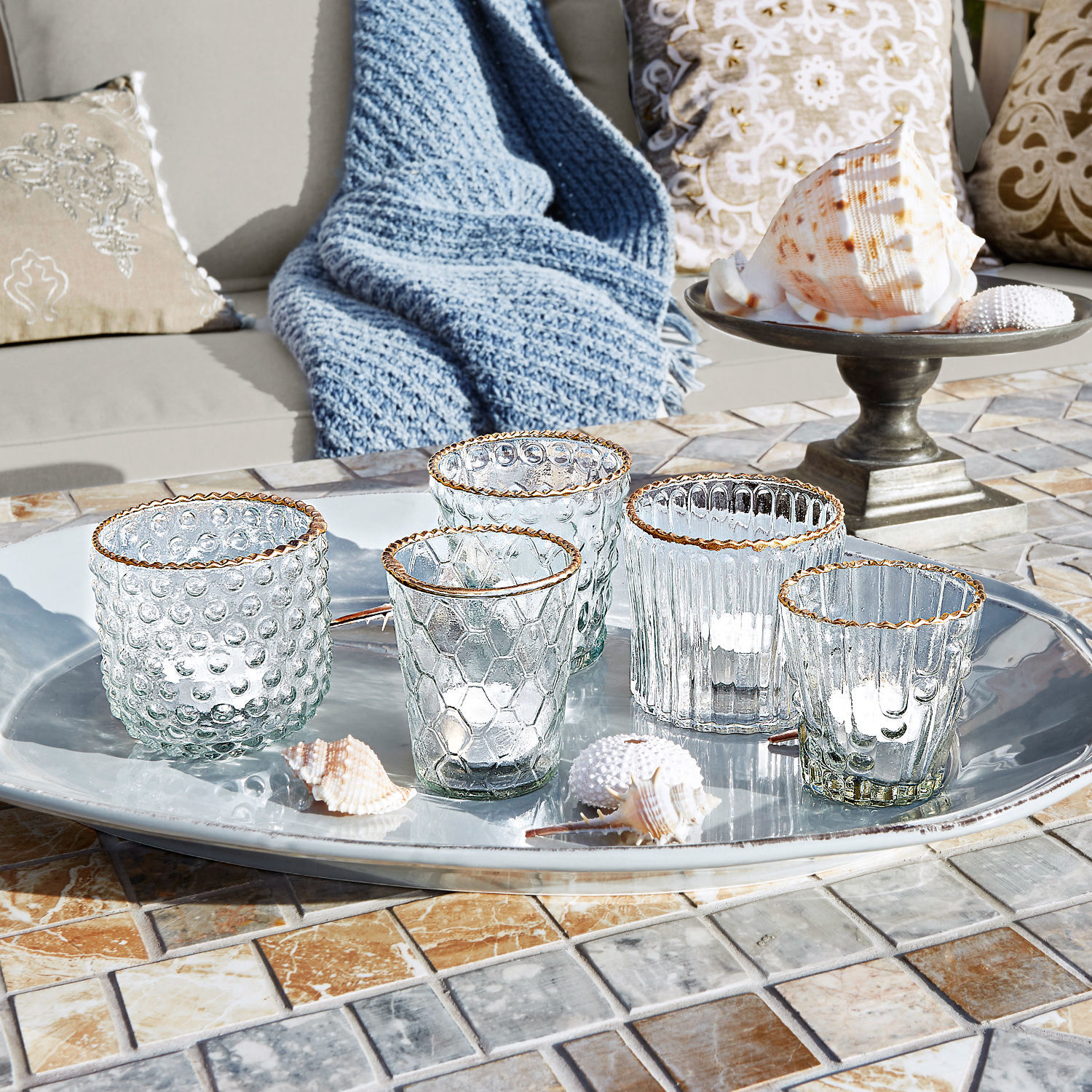 Set di 5 portalumini Jarnac Set di cinque portacandele in vetro con bordo dorato su vassoio argentato su tavolo a mosaico