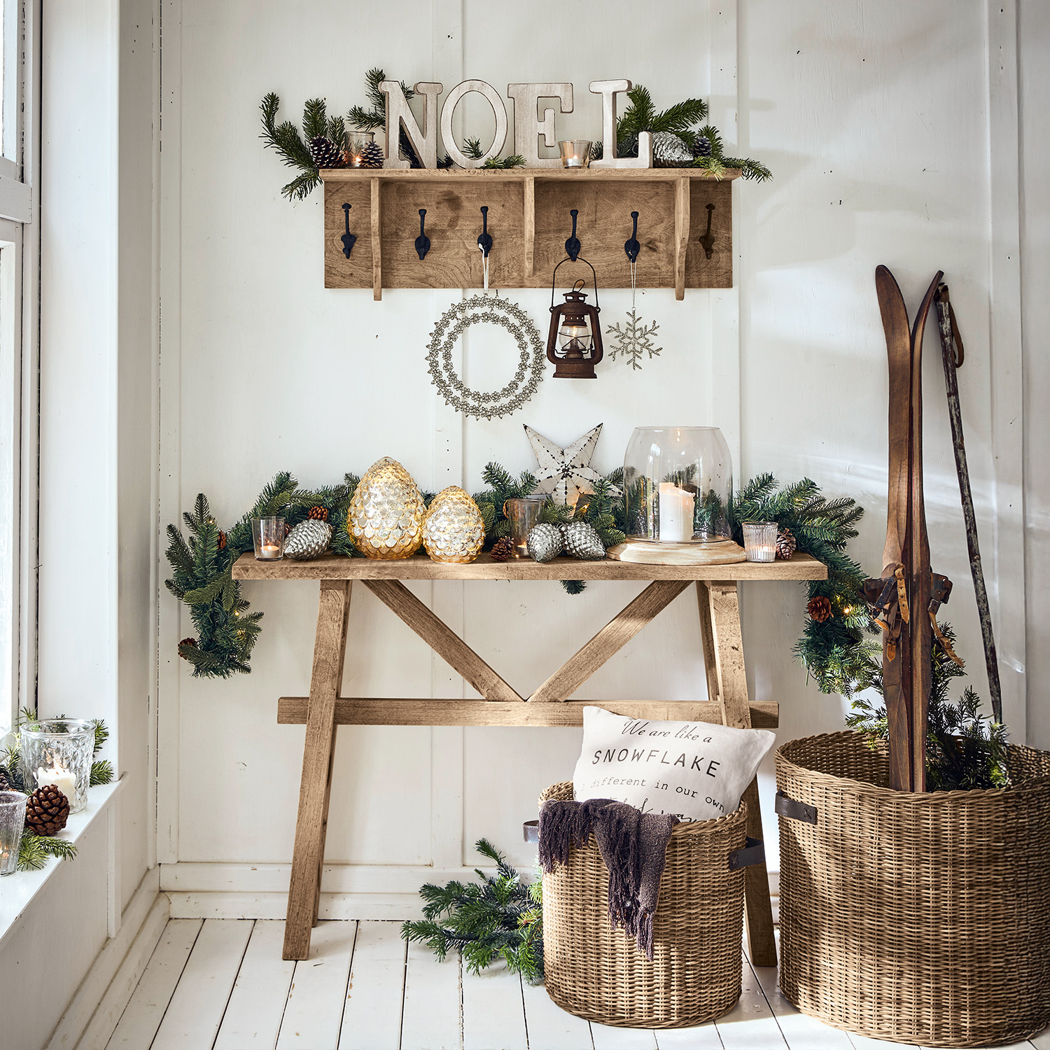 Tavolo in legno e appendiabiti con decorazioni natalizie, lanterna e cesti in vimini con sci