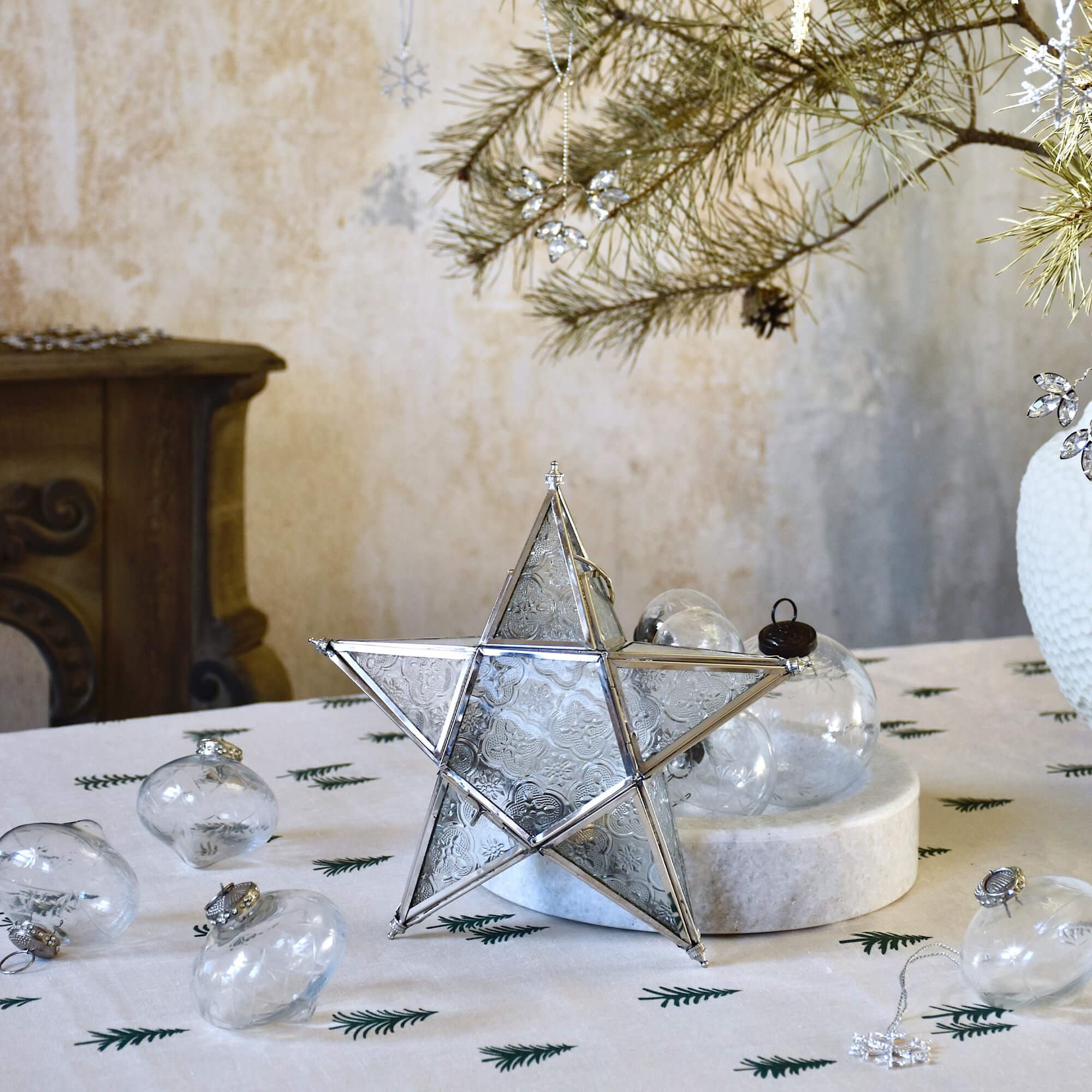 Stella decorativa in vetro e metallo su tavola natalizia con ornamenti e rami di pino