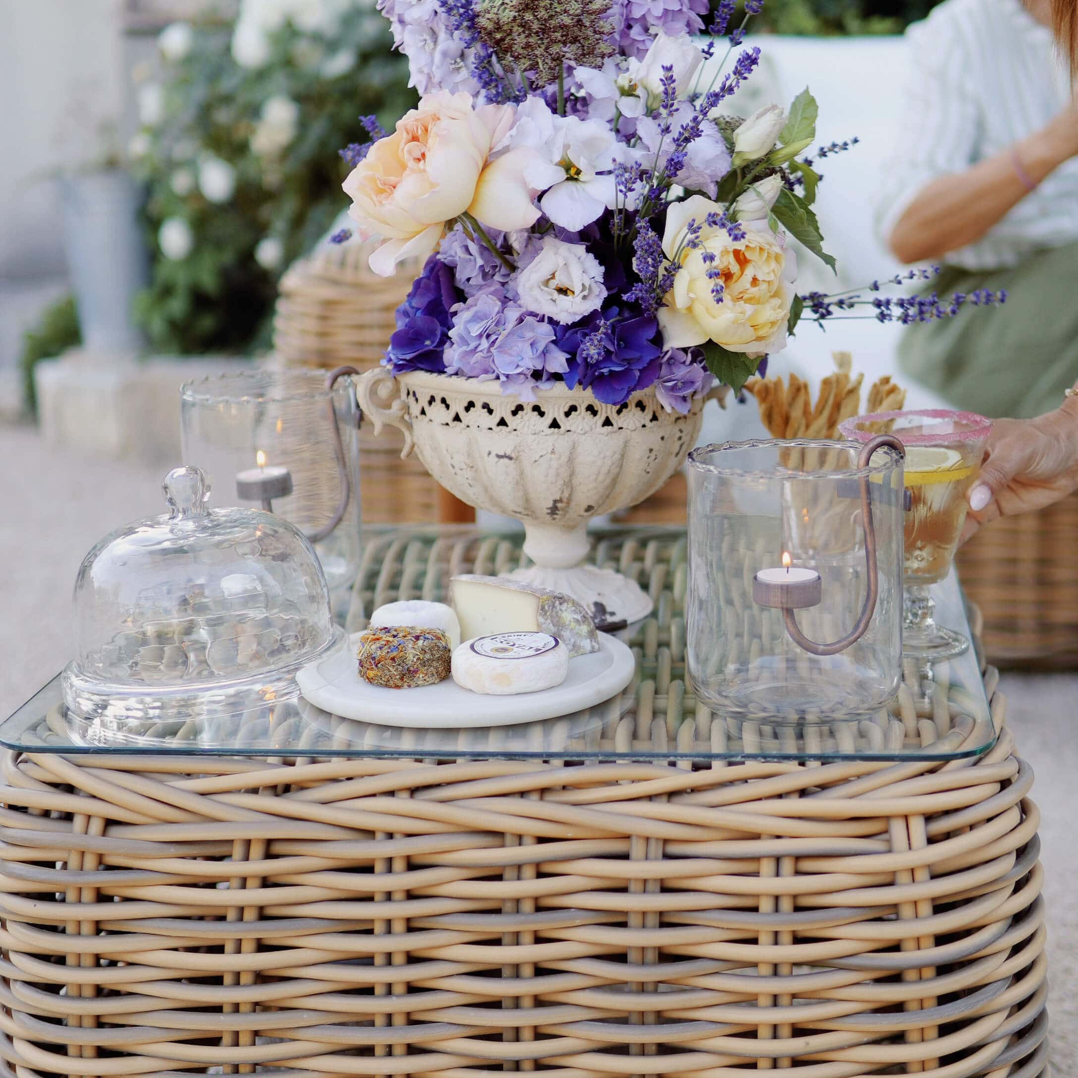 Composizione decorativa di lavanda e rose in vaso di ceramica bianca su tavolo in rattan con formaggi