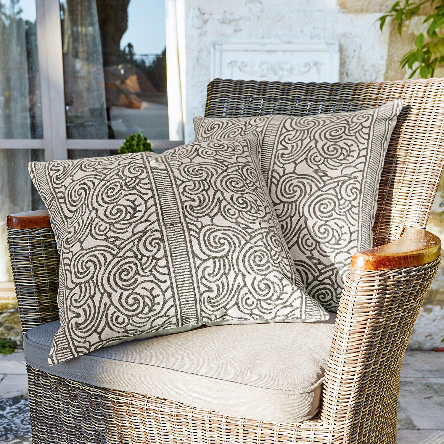 Coppia di copricuscini Ensis Due cuscini decorativi in cotone beige con motivo marrone su poltrona in vimini su terrazza