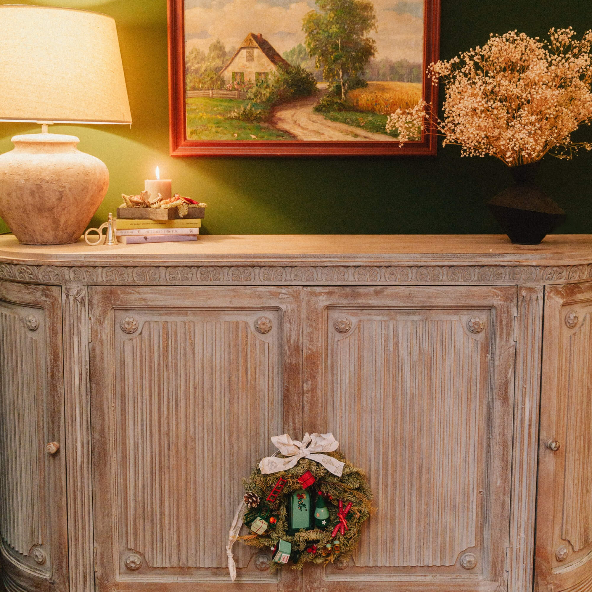 Credenza rustica in legno con corona natalizia decorativa e lampada su parete verde