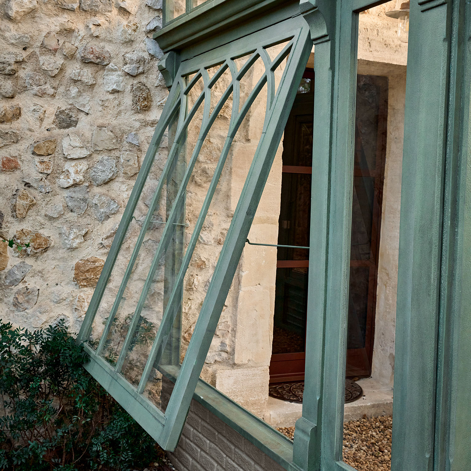 Finestra verde in metallo con motivo decorativo su muro di pietra e piante sullo sfondo