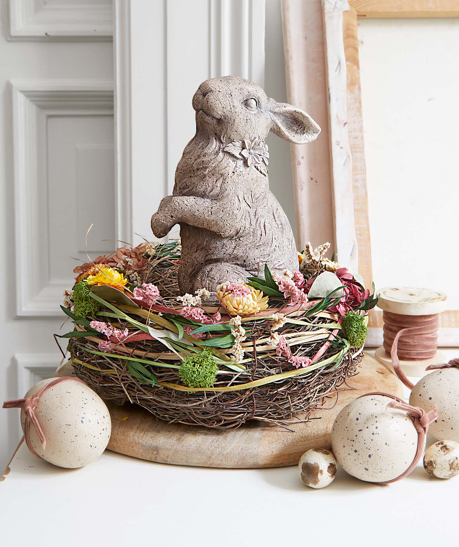 Coniglio decorativo in cemento in nido con fiori secchi e uova decorative per la primavera
