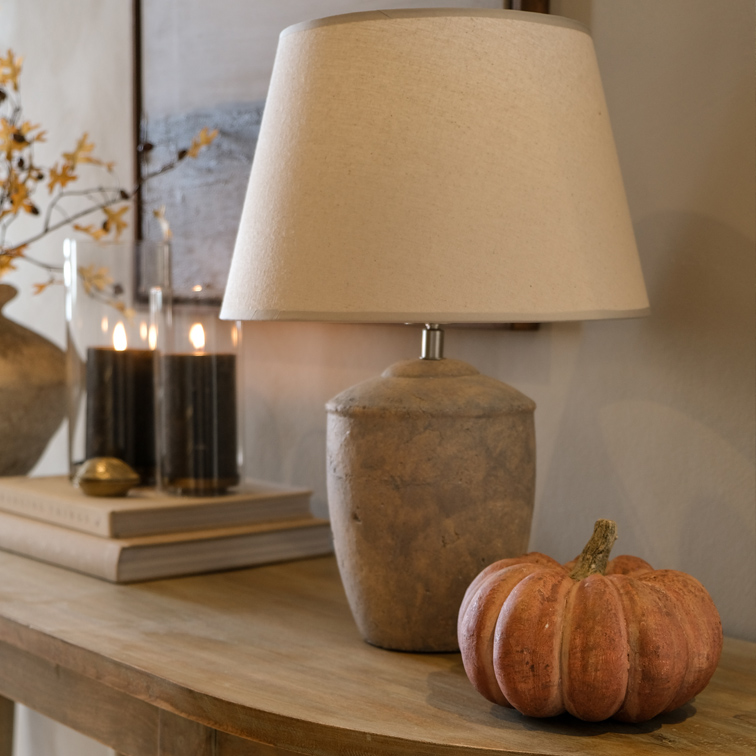 Lampada da tavolo con paralume beige e base in pietra su tavolo in legno con decorazione di zucca
