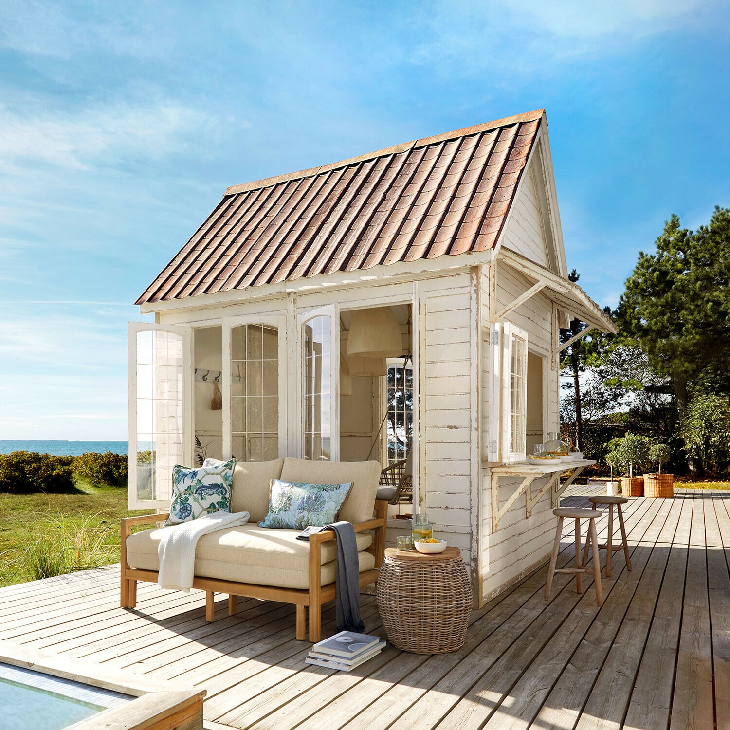 Casetta da giardino Stormhavn Gazebo in legno bianco con tetto rosso e divano beige su terrazza in legno vista mare