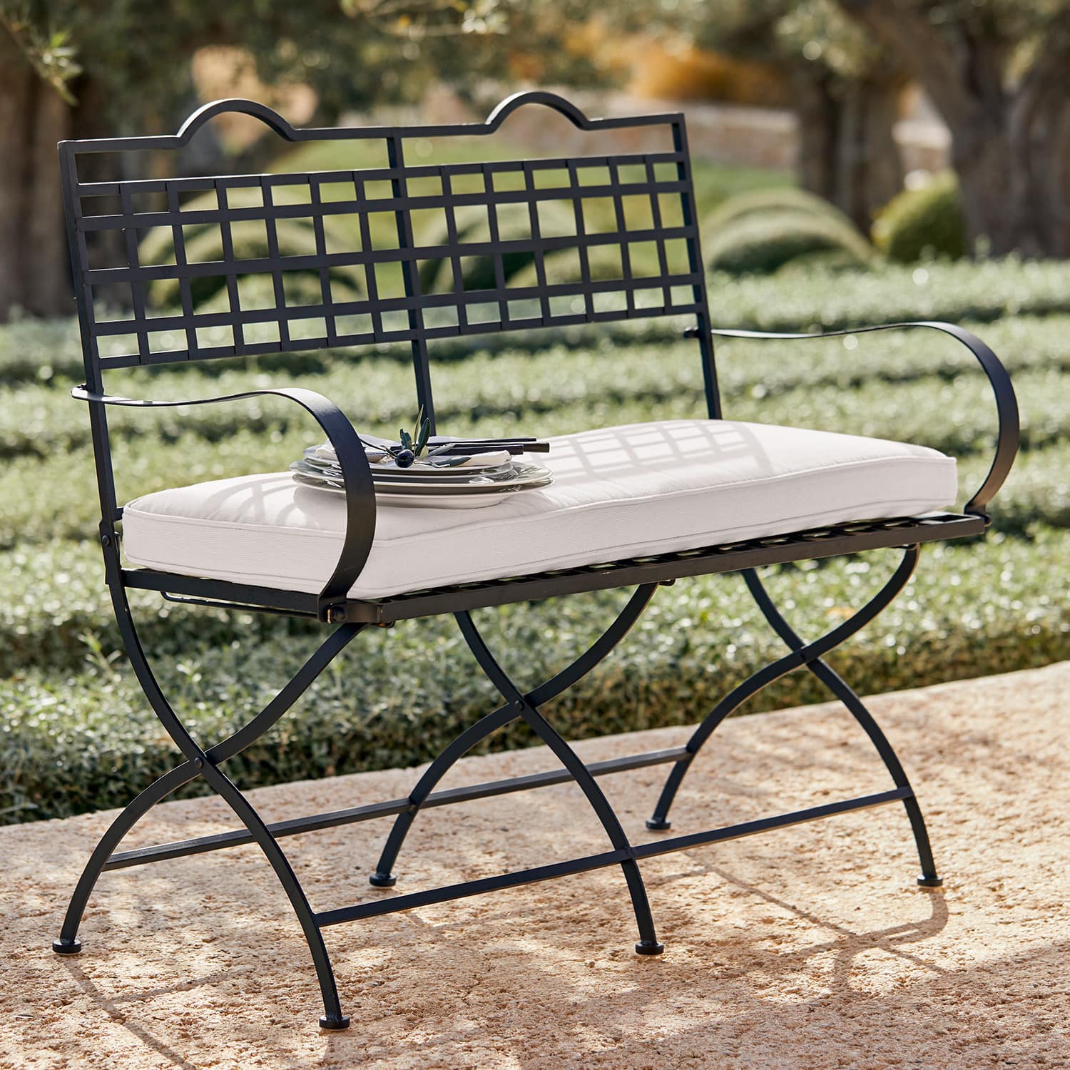 Panca Terell Panca da giardino in metallo nero con cuscino bianco su terrazza in pietra all'aperto