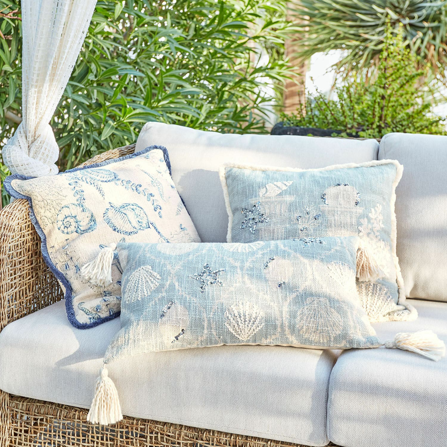 Set di 3 copricuscini Calerand Set di cuscini decorativi blu e beige con motivi di conchiglie e stelle marine su divano in rattan