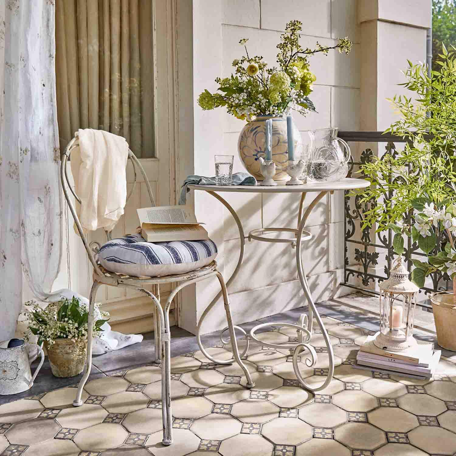 Tavolo e sedia in metallo bianco con cuscino a righe su terrazza con fiori e lanterna decorativa