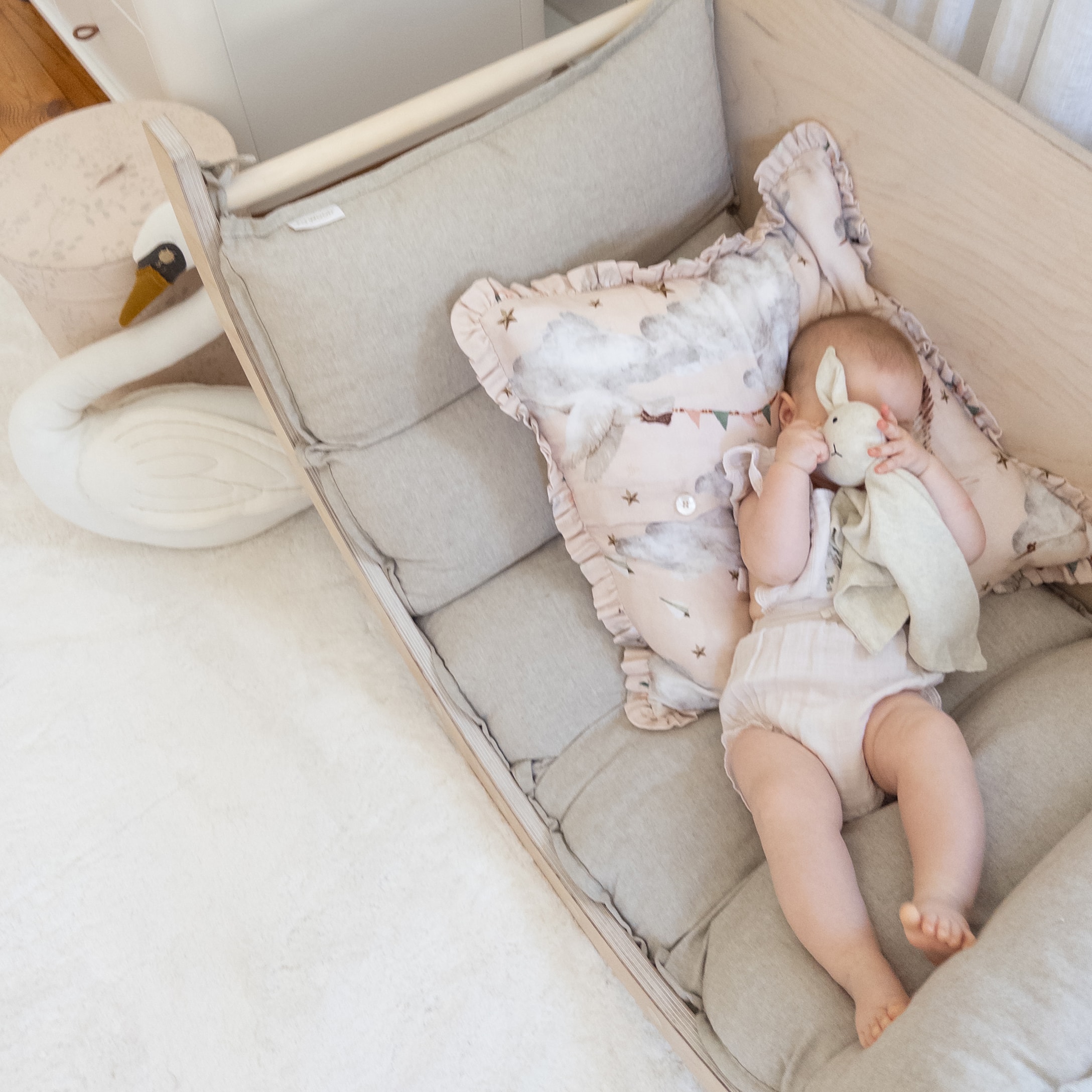Bambino sdraiato su materasso grigio morbido con cuscino a motivi pastello e peluche coniglio