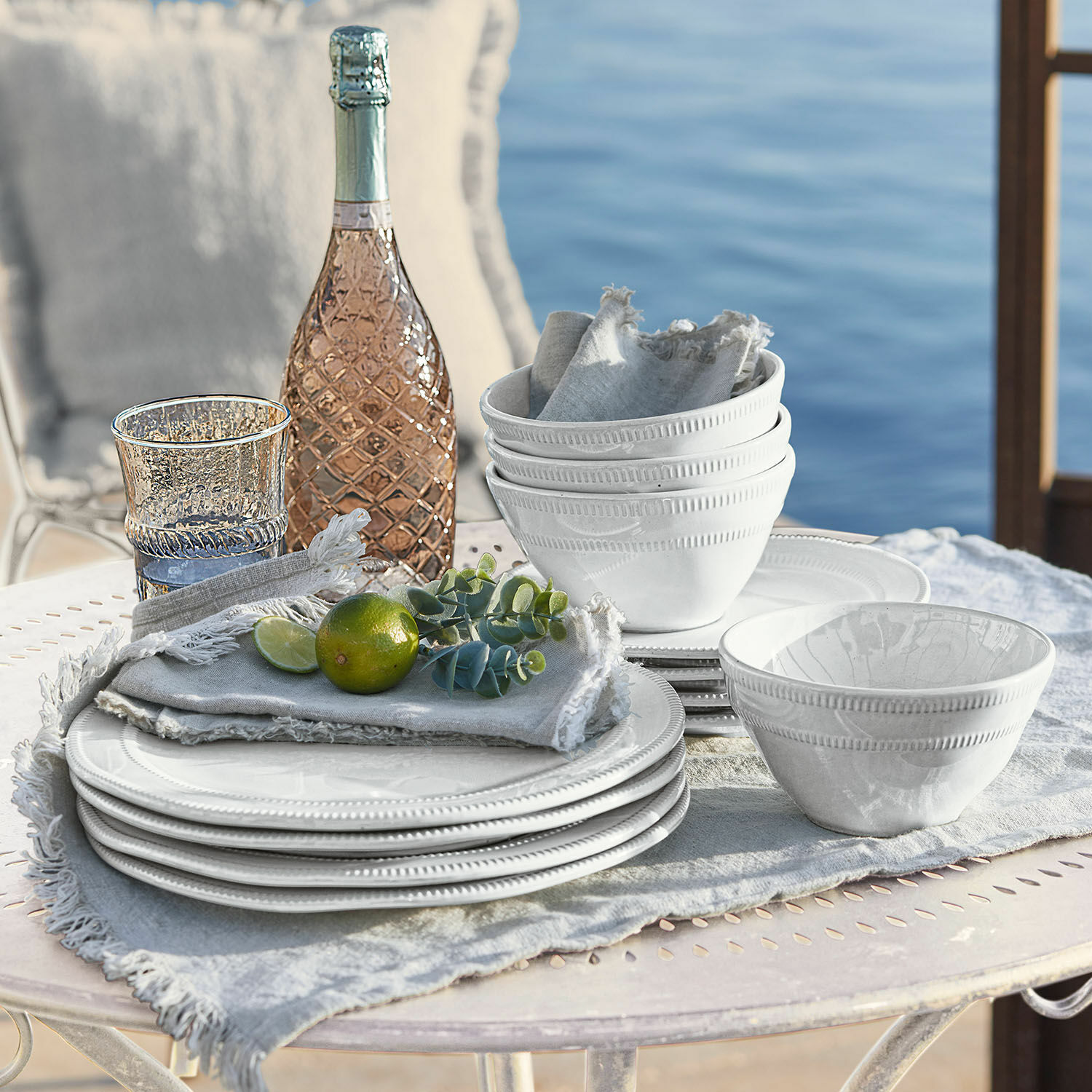 Set di 12 stoviglie Alentejo Set di stoviglie in ceramica bianca con piatti e ciotole su tessuto chiaro vicino all'acqua