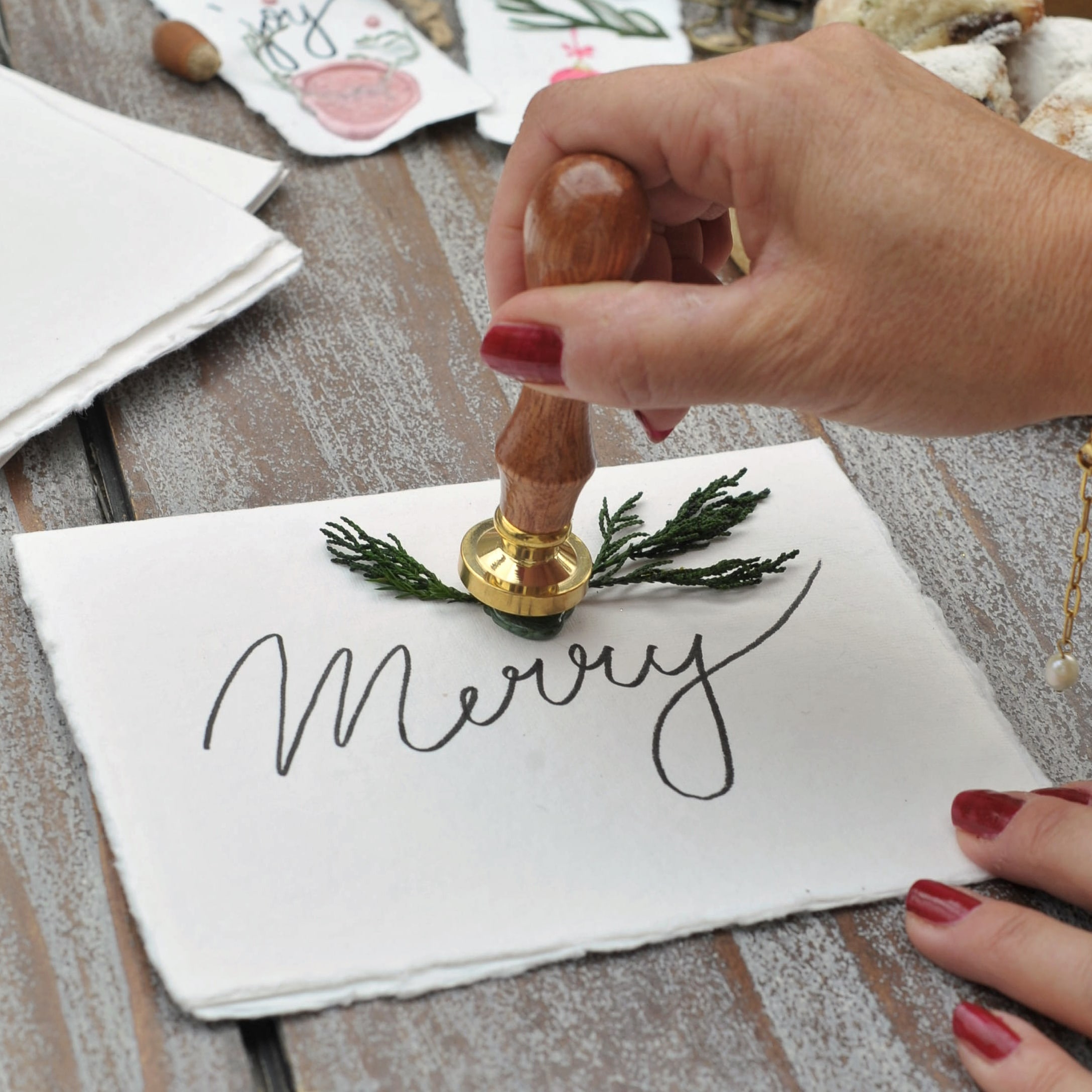 Mano con smalto rosso usa sigillo in legno per decorare cartolina bianca con scritta Merry