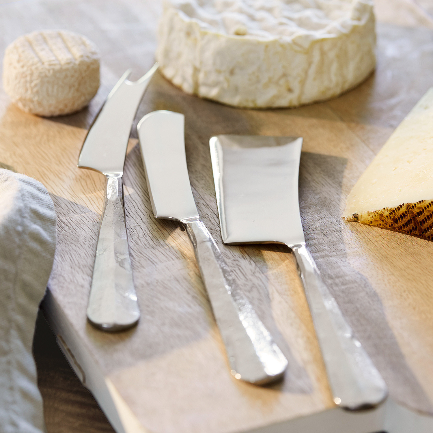 Set di 3 coltelli per formaggi Mondevert Set di tre coltelli per formaggio in acciaio inox su tagliere in legno con formaggi assortiti