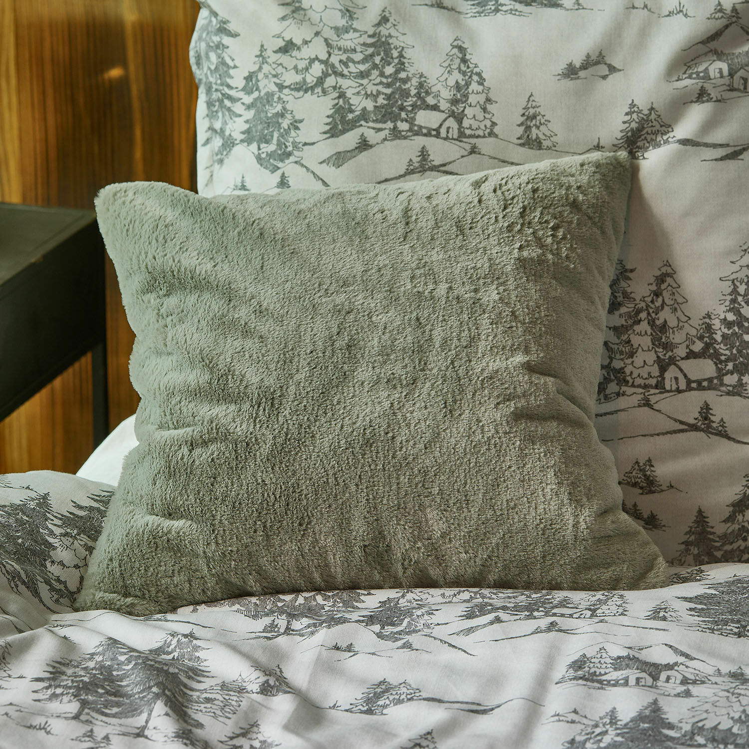 Copricuscino Léorienne Morbido cuscino verde in peluche su letto con copripiumino a motivi grigi di alberi e case