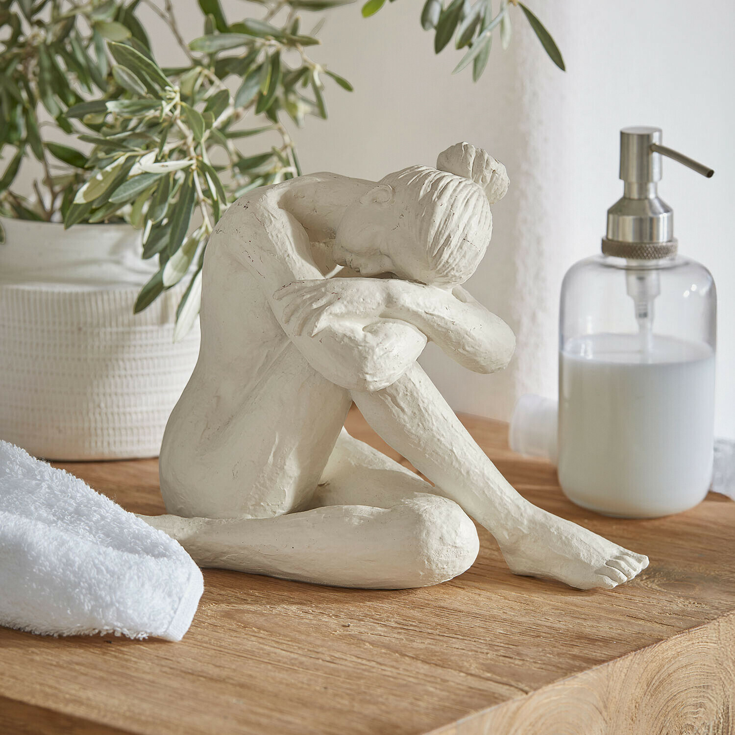 Statuina Savigné Scultura bianca di donna seduta con testa sulle ginocchia piegate su piano in legno in bagno