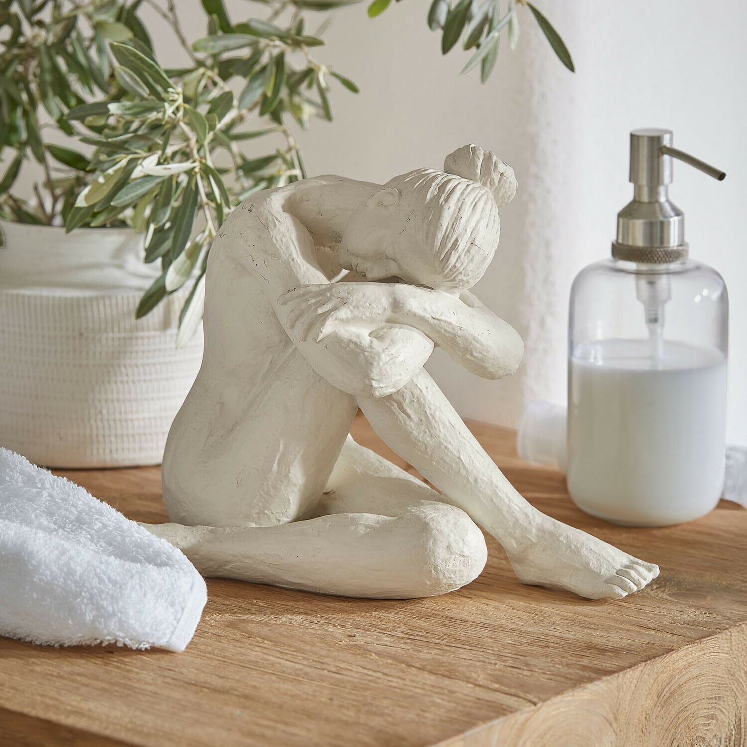 Statuina Savigné Scultura bianca di donna seduta con testa sulle ginocchia piegate su piano in legno in bagno