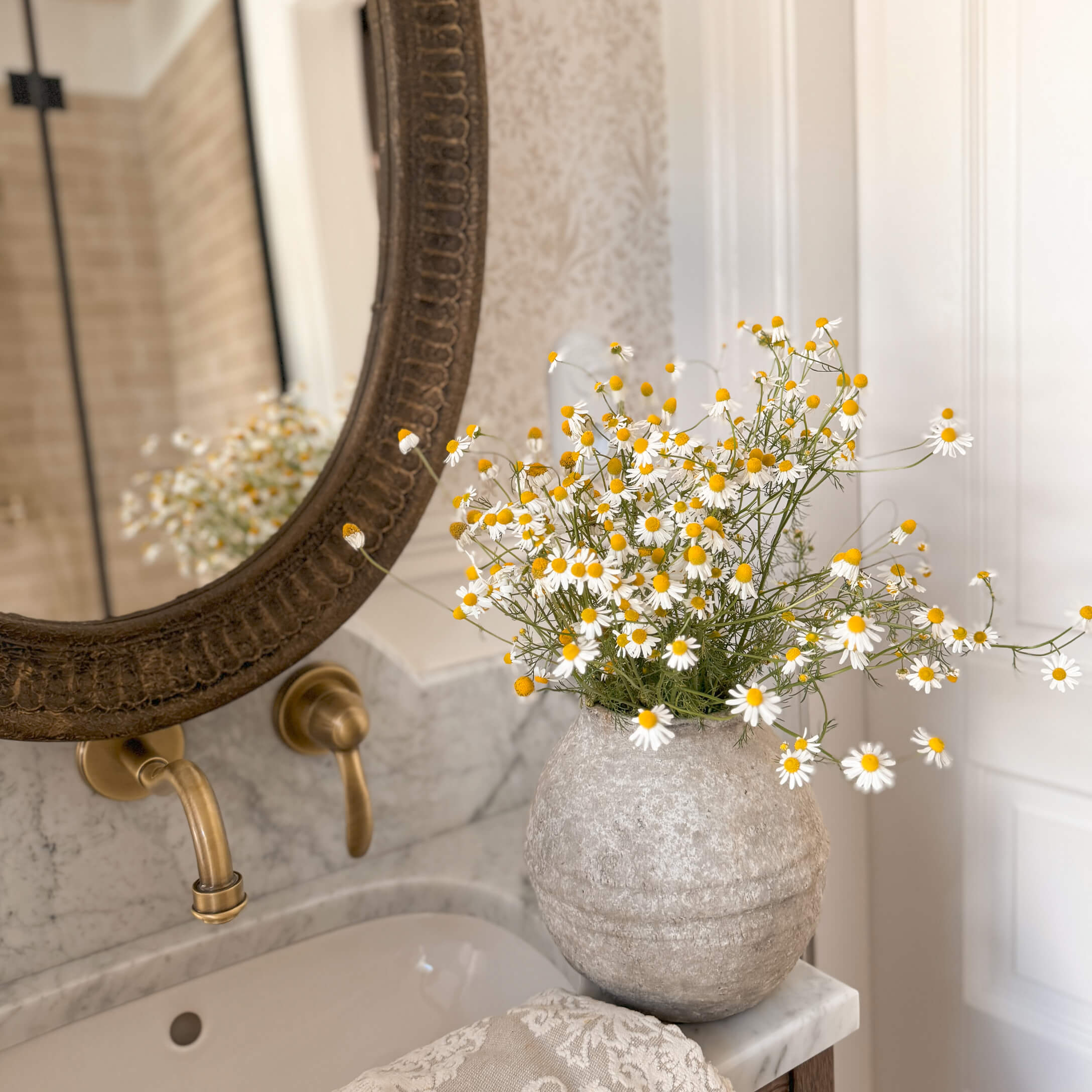 Vaso in pietra grigia con fiori bianchi e gialli su lavabo in marmo in bagno elegante