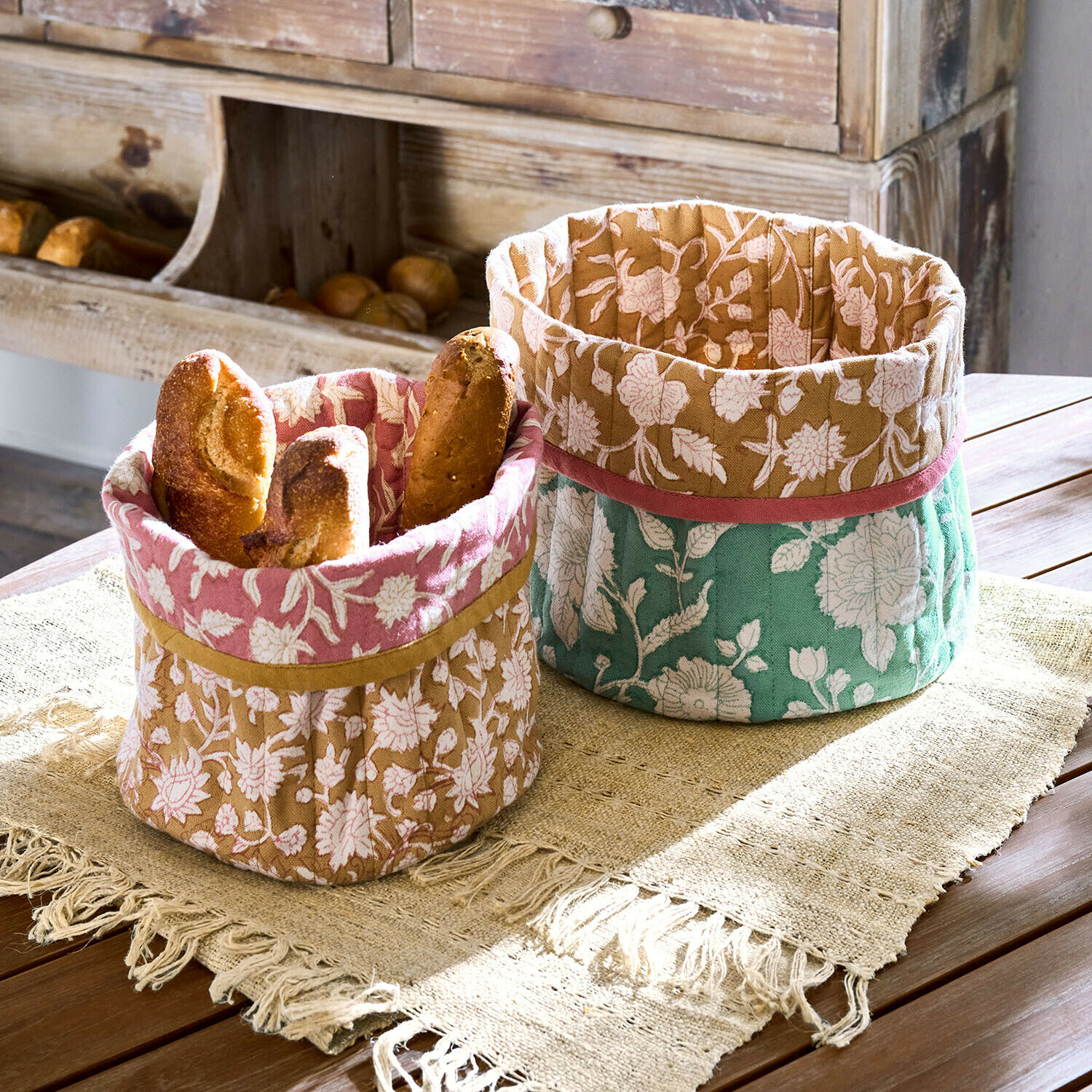 Due ceste decorative in cotone con motivo floreale rosa, marrone e verde per pane su tavolo in legno