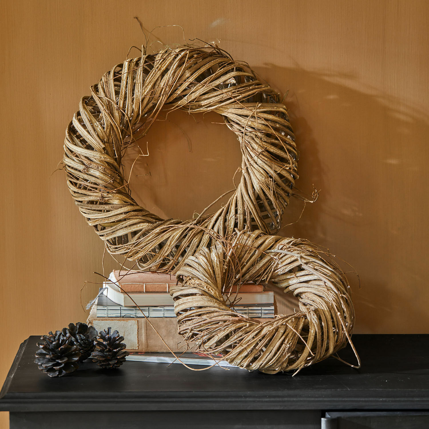 Coppia di ghirlande Lunéor Corone decorative in vimini naturale beige su tavolo nero con libri impilati