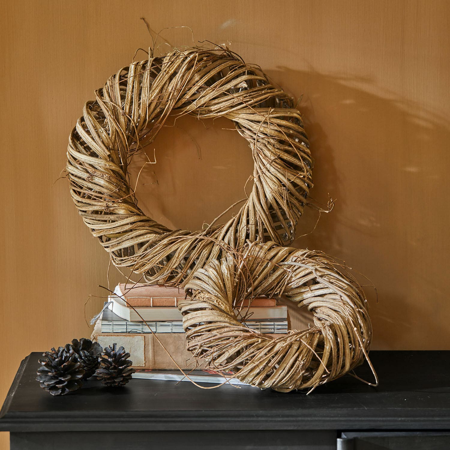 Coppia di ghirlande Lunéor Corone decorative in vimini naturale beige su tavolo nero con libri impilati