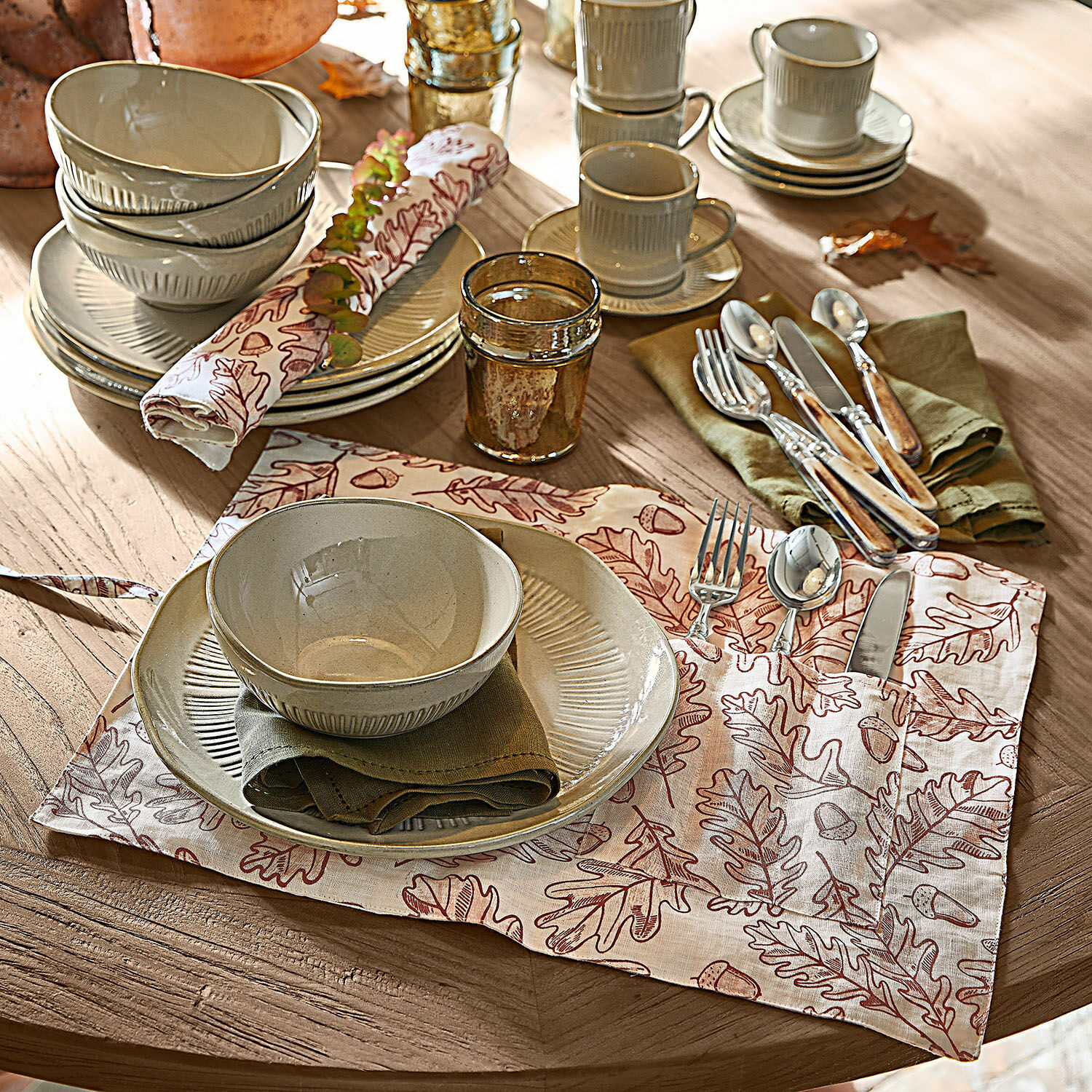 Coppia di tovagliette Qubinal Set di piatti e ciotole in ceramica beige su tavolo in legno con tovaglietta decorativa a foglie