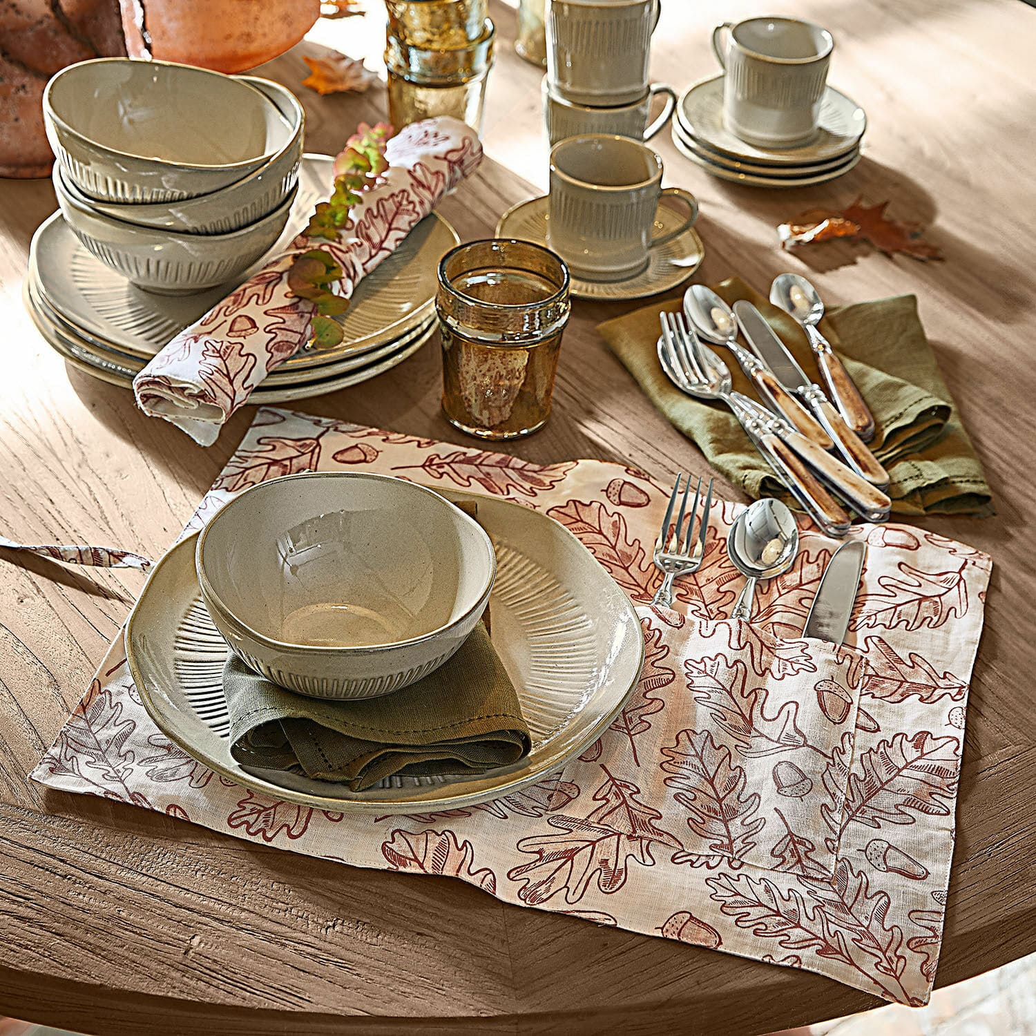 Coppia di tovagliette Qubinal Set di piatti e ciotole in ceramica beige su tavolo in legno con tovaglietta decorativa a foglie