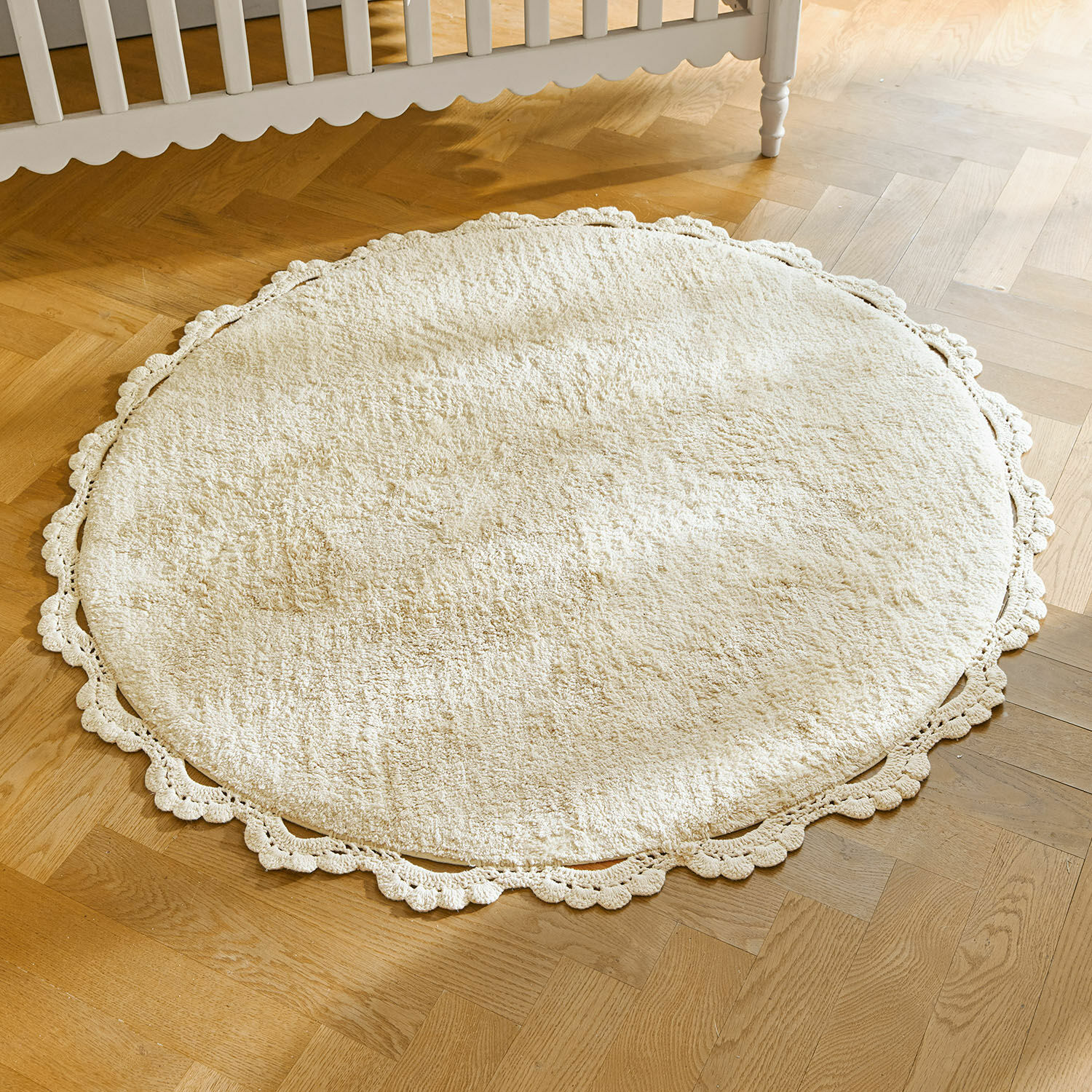 Tappeto Arash Tappeto rotondo crema in cotone con bordo in pizzo su pavimento in legno chiaro, decorazione d'interni
