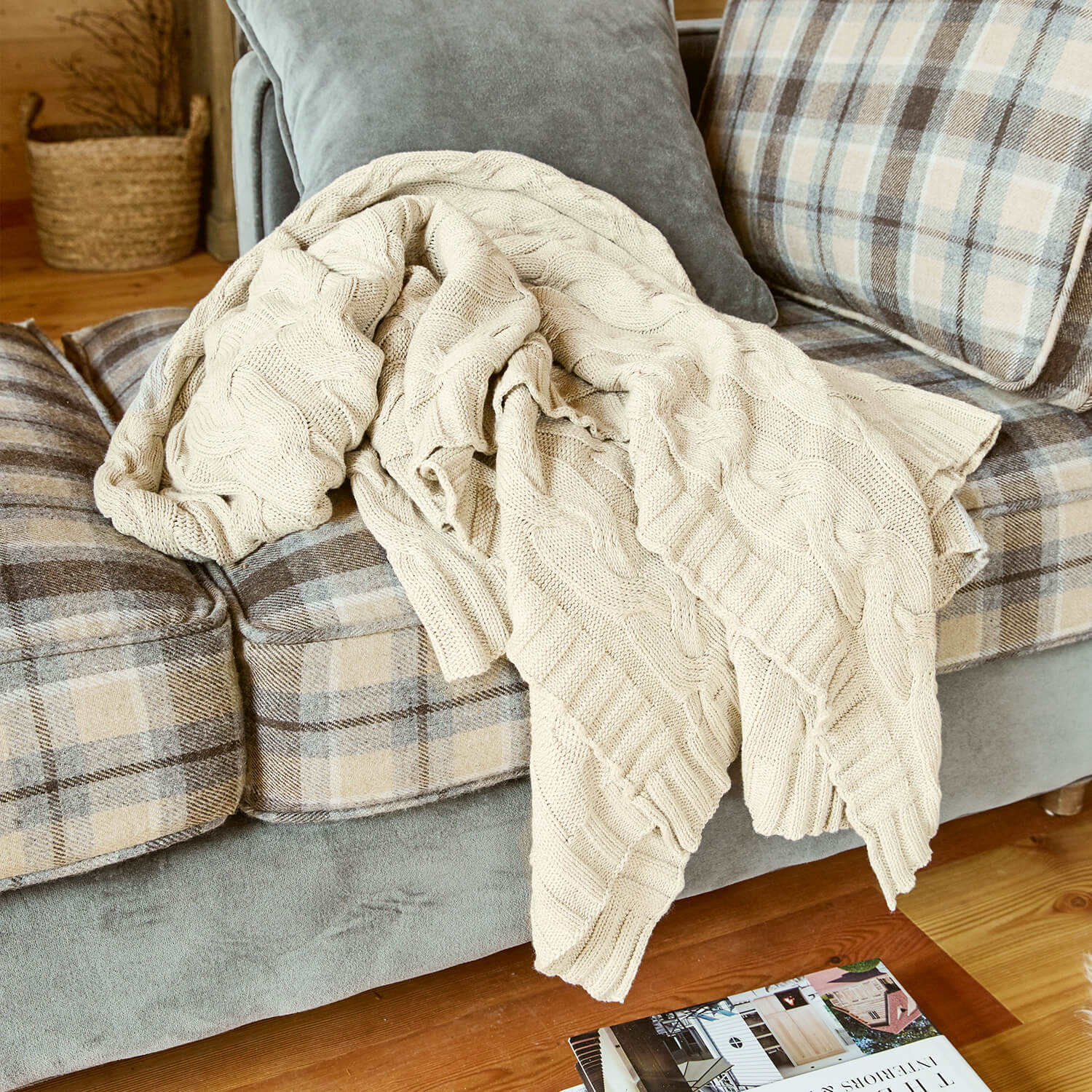 Coperta beige lavorata a maglia con motivo a treccia su divano grigio a quadri beige in soggiorno